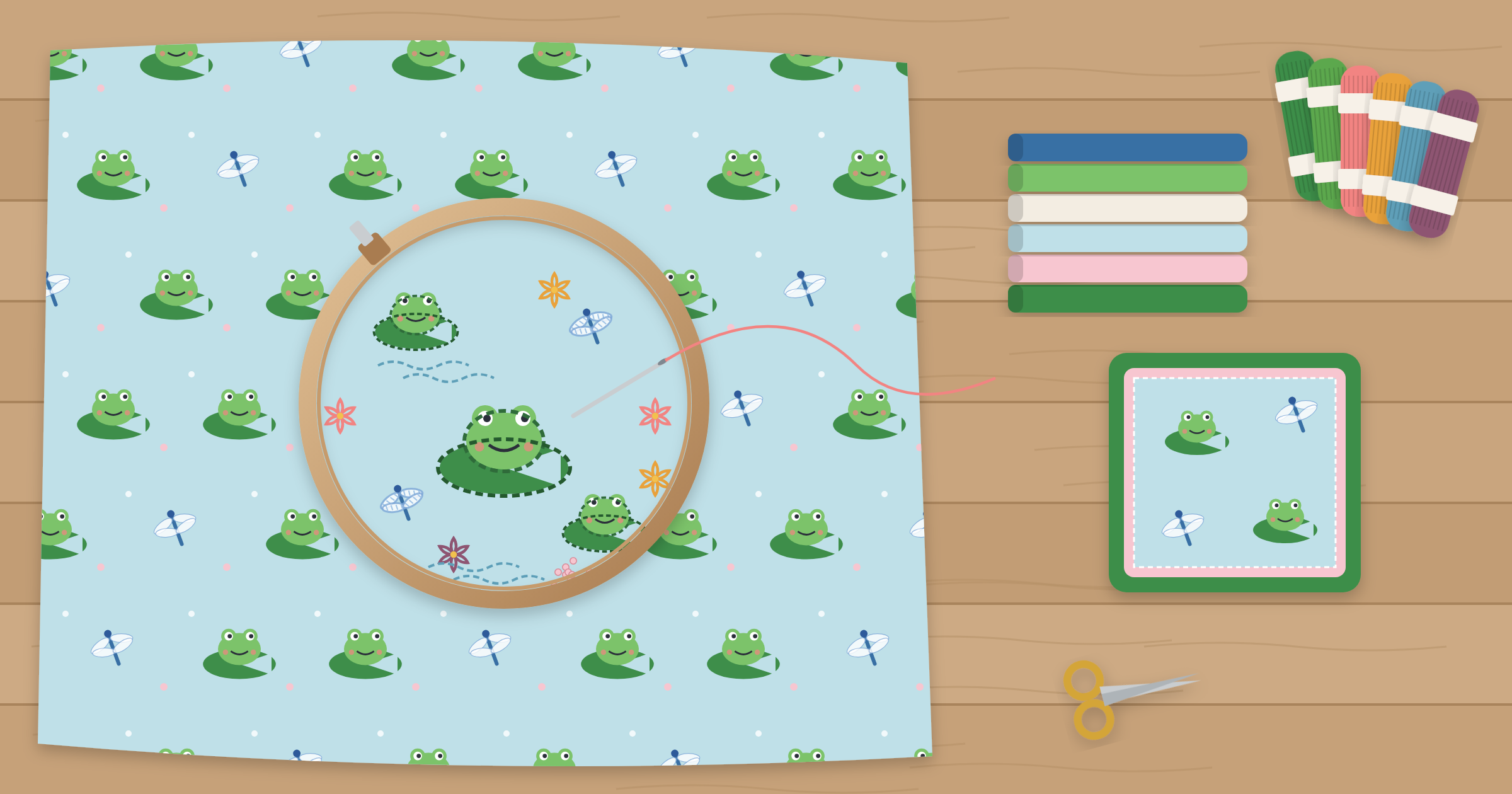 Frog and dragonfly novelty print fabric with embroidery added in a hoop, beside coordinating solid fabrics, embroidery floss, and a pillow cover framing the novelty print with solid borders