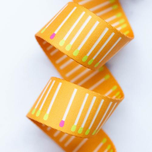 Meet Match Goldenrod 1.5-inch polyester webbing by Rashida Coleman-Hale featuring white matchstick-style lines with pink and lime green accents on a goldenrod orange background.