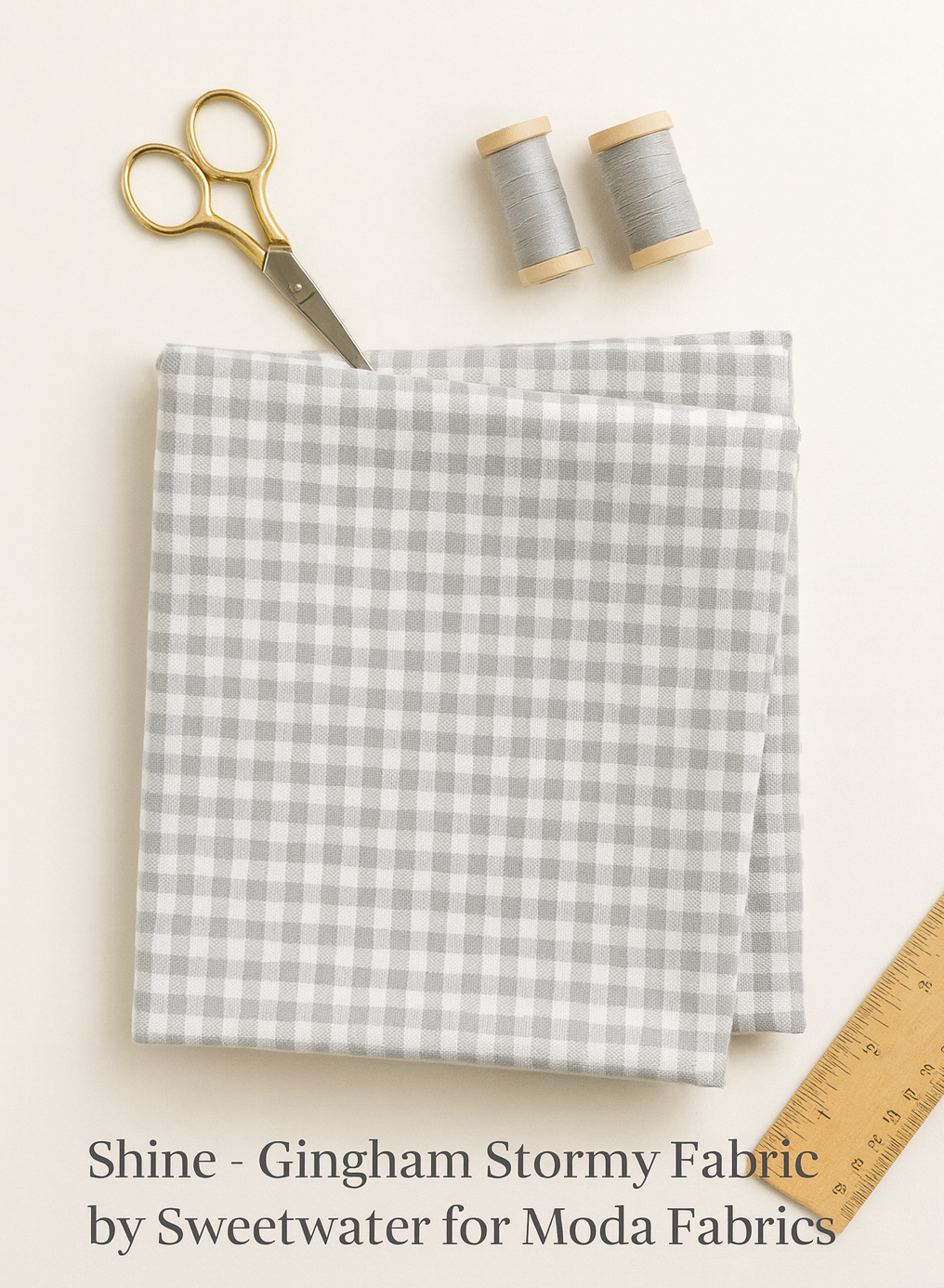 folded gray gingham fabric with scissors, gray thread spools, and a ruler on a light background.