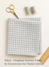 folded gray gingham fabric with scissors, gray thread spools, and a ruler on a light background.