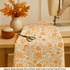 A cozy autumn-inspired sewing corner featuring the Agatha Road – Harvest Floral Ghost Multi Fabric by Fig Tree & Co for Moda Fabrics displayed as a table runner in progress, surrounded by thread spools, scissors, and fall leaves on a wooden sewing table with warm ambient lighting.