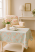 A cozy cottage-style living room featuring Muse - Flower Picking Sky Fabric by 3 Sisters for Moda Fabrics, used as a tablecloth beside a floral armchair, vase of pink roses, and warm sunlight through cream curtains, creating a soft, romantic ambiance.