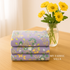 A cozy sewing room scene featuring folded Sherbet Sunshine Lavender Floral Flannel Fabric by Corey Yoder for Moda Fabrics beside a vase of yellow flowers, radiating warmth and comfort.