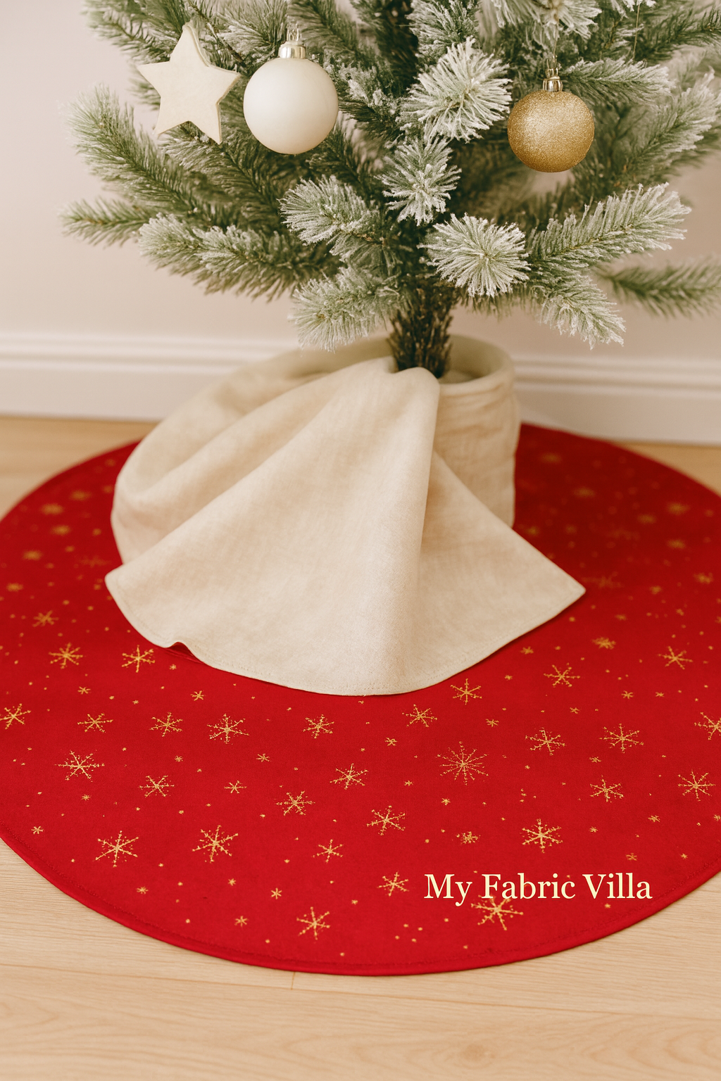 A decorated Christmas tree stands in a cozy living room, with a red ombré tree skirt made from Ombre Flurries Metallic fabric by V and Co. for Moda Fabrics, featuring shimmering gold snowflakes and a “My Fabric Villa” watermark on the lower right.