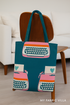 A cozy creative studio scene showcasing a tote bag and decorative pillow made from Ruby Star Society’s Best Day Ever Typewriters Teal Canvas by Melody Miller for Moda Fabrics, featuring pink retro typewriters on a deep teal background, with a “My Fabric Villa” watermark in the bottom-right corner for branding.