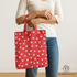 A woman holding a tote bag made from 30s Playtime 2025 Perky Posies Scarlet Fabric by Linzee McCray for Moda Fabrics, featuring white floral prints on a bright red cotton background, with cream straps and a “My Fabric Villa” watermark in the bottom right corner.