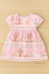 A pastel pink baby dress made from Storybook Forest Bunnies & Deer Stripe fabric by Timeless Treasures, featuring playful deer, bunnies, and trees in a stripe pattern. The short-sleeved dress with a gathered skirt is displayed on a light wooden background under soft white lighting, with a small “My Fabric Villa” watermark in the bottom right corner.