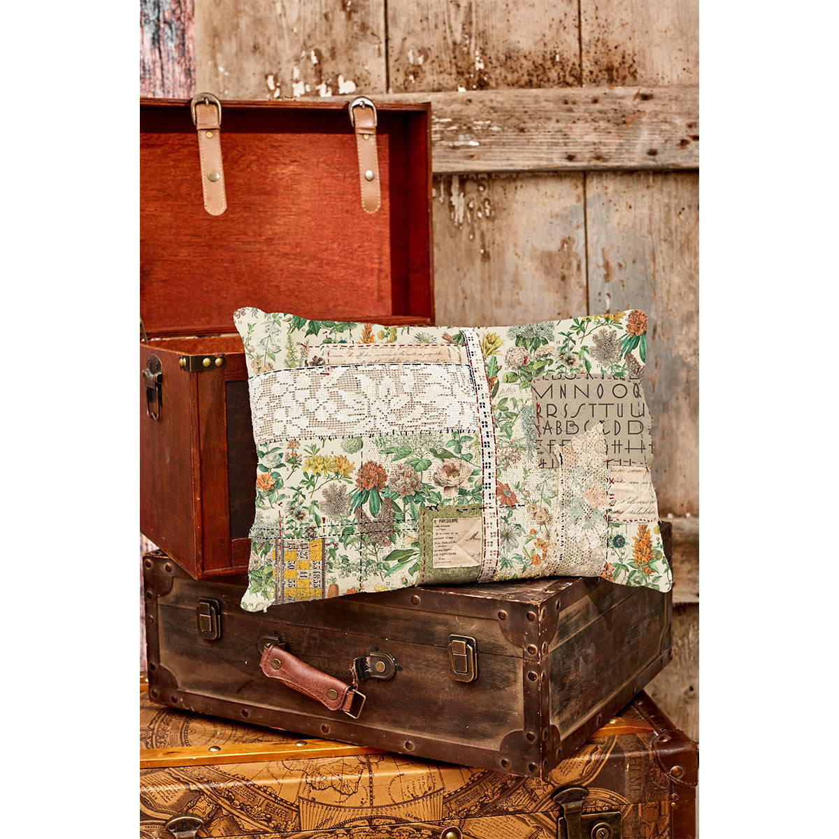 Decorative patchwork pillow sewn with Tim Holtz Palette Orange Botanical cotton canvas fabric, featuring vintage botanical illustrations in warm earthy tones, displayed on antique travel trunks in a rustic setting.