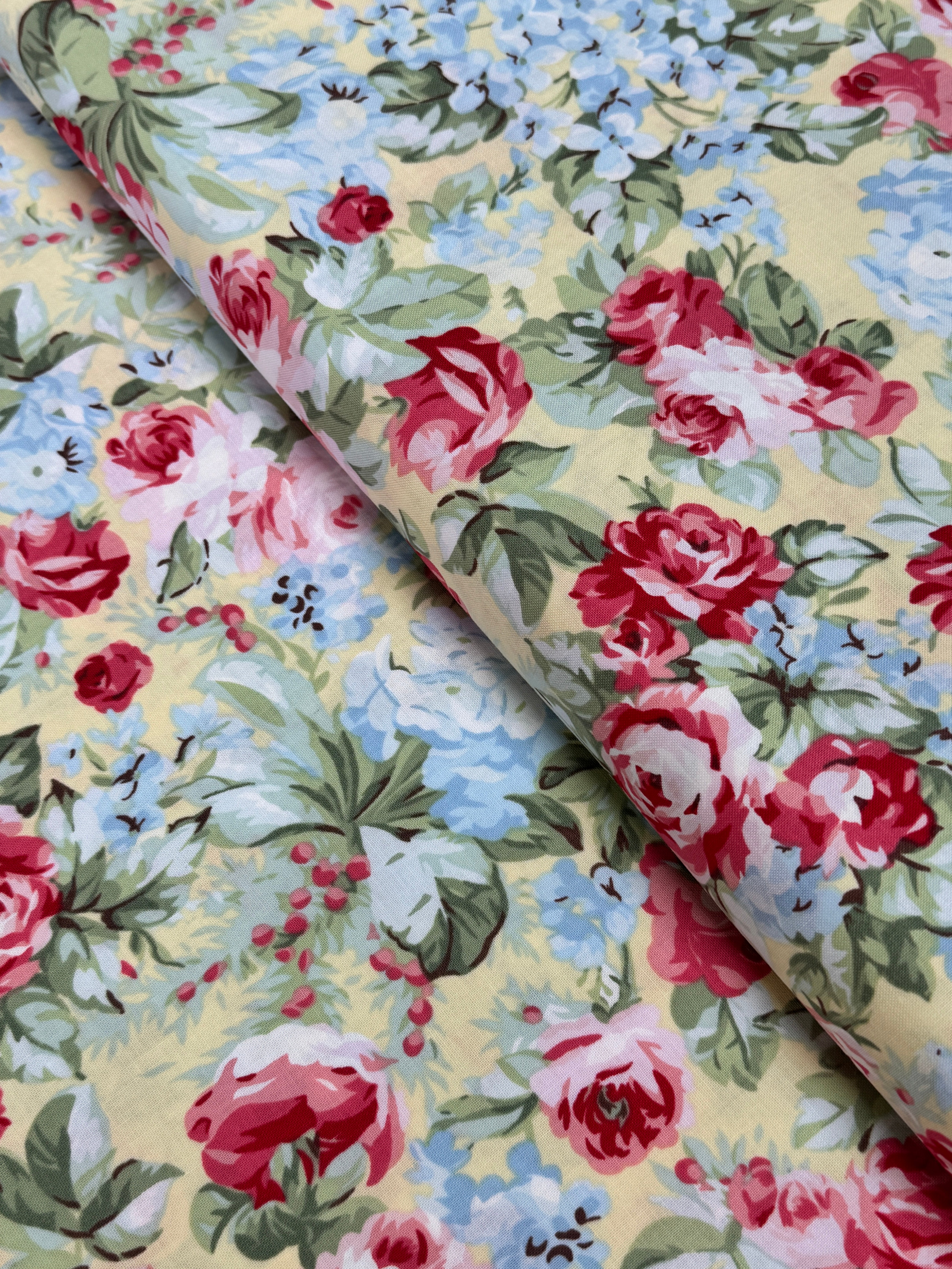 Floral cotton fabric featuring pink roses, blue hydrangeas, and delicate blossoms on a soft butter yellow background from the Simply Chic collection by Anna Stuart for Benartex.