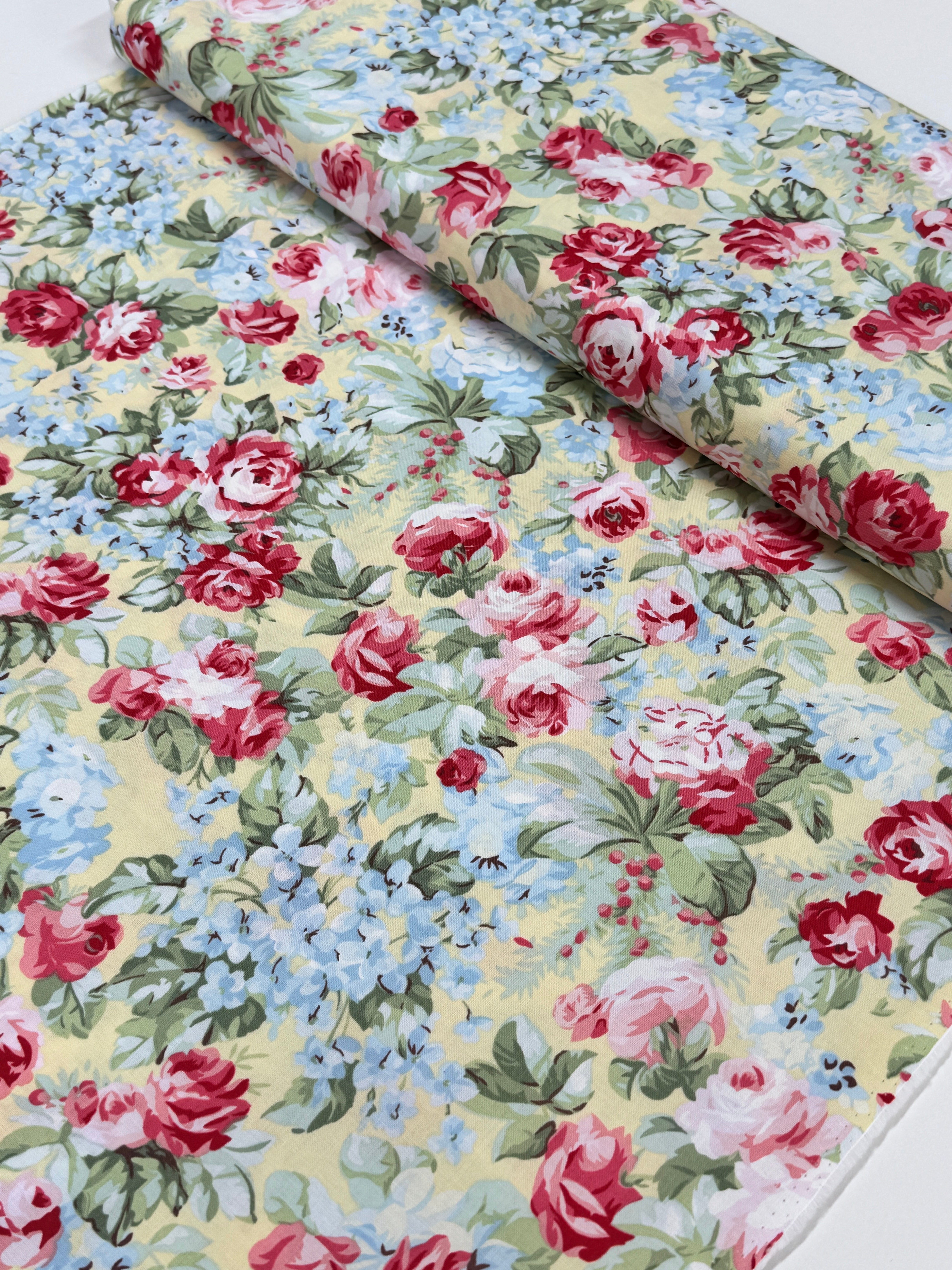 Floral cotton fabric featuring pink roses, blue hydrangeas, and delicate blossoms on a soft butter yellow background from the Simply Chic collection by Anna Stuart for Benartex.