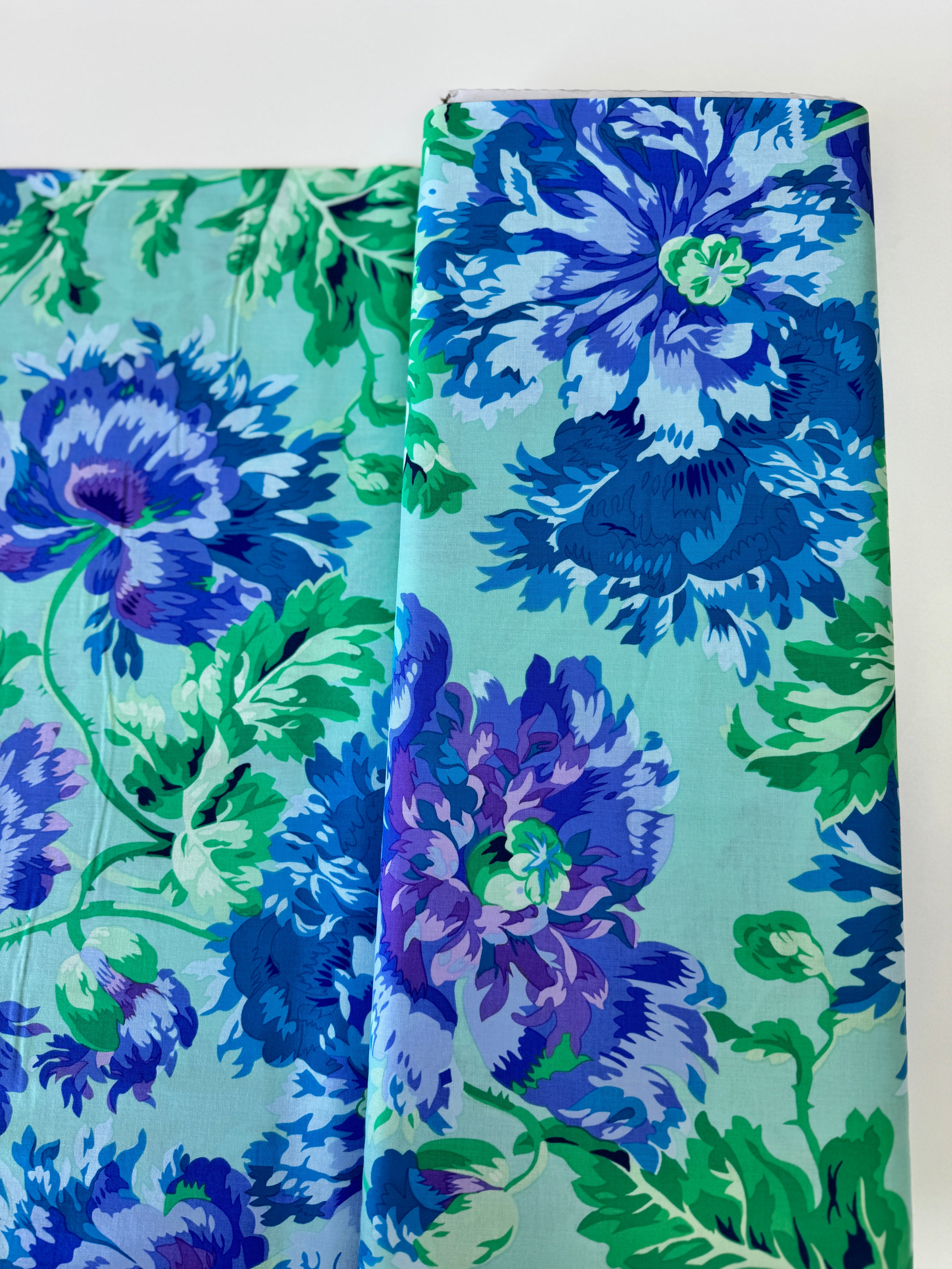 Kaffe Fassett Collective Garden Party Celadon fabric by Philip Jacobs for Free Spirit Fabrics featuring large blue and purple floral blooms with green leaves on a celadon background.