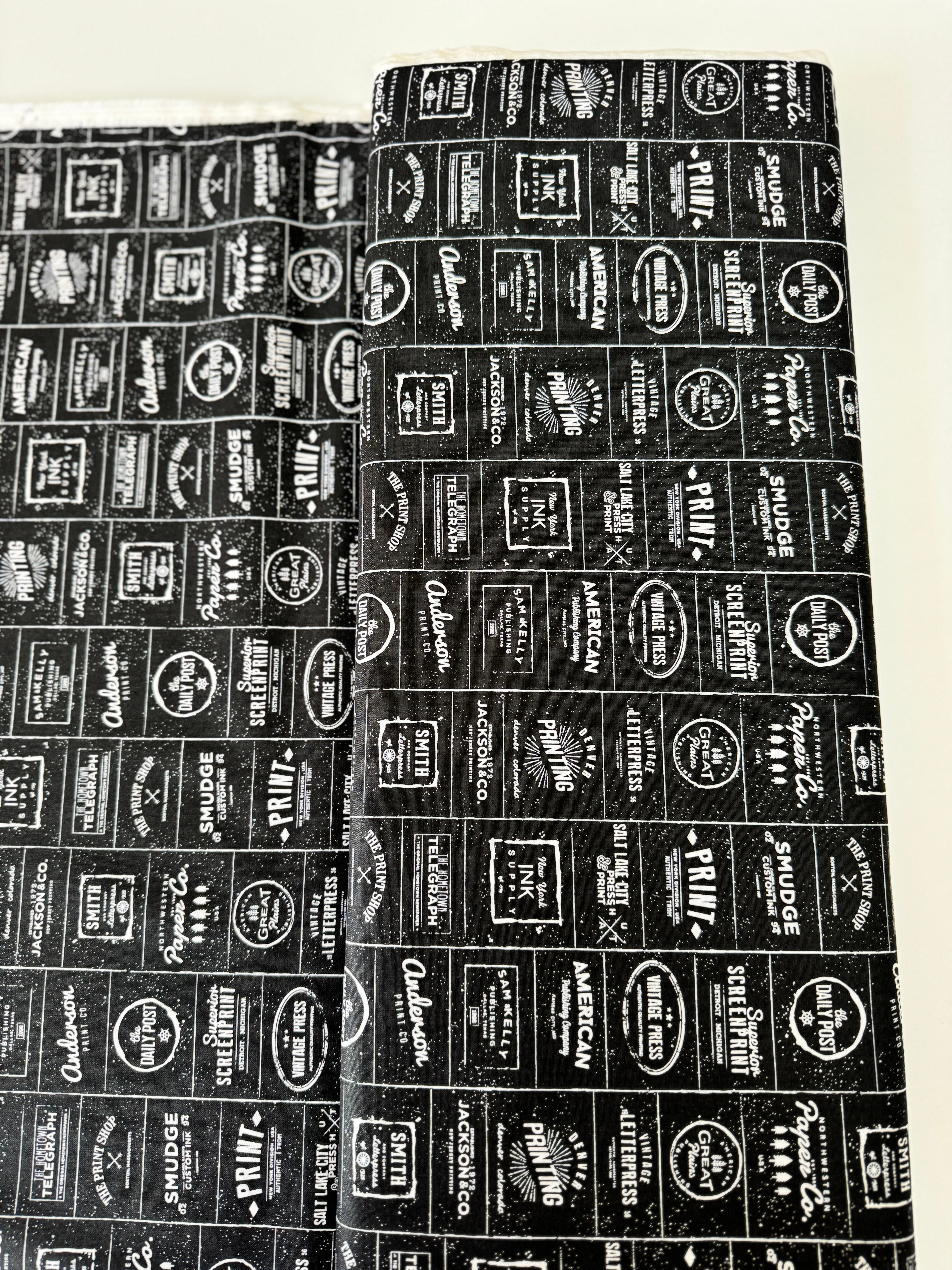 The Print Shop Modern Logos Black fabric by Sweetwater for Moda Fabrics featuring white vintage typography logos on a black background.