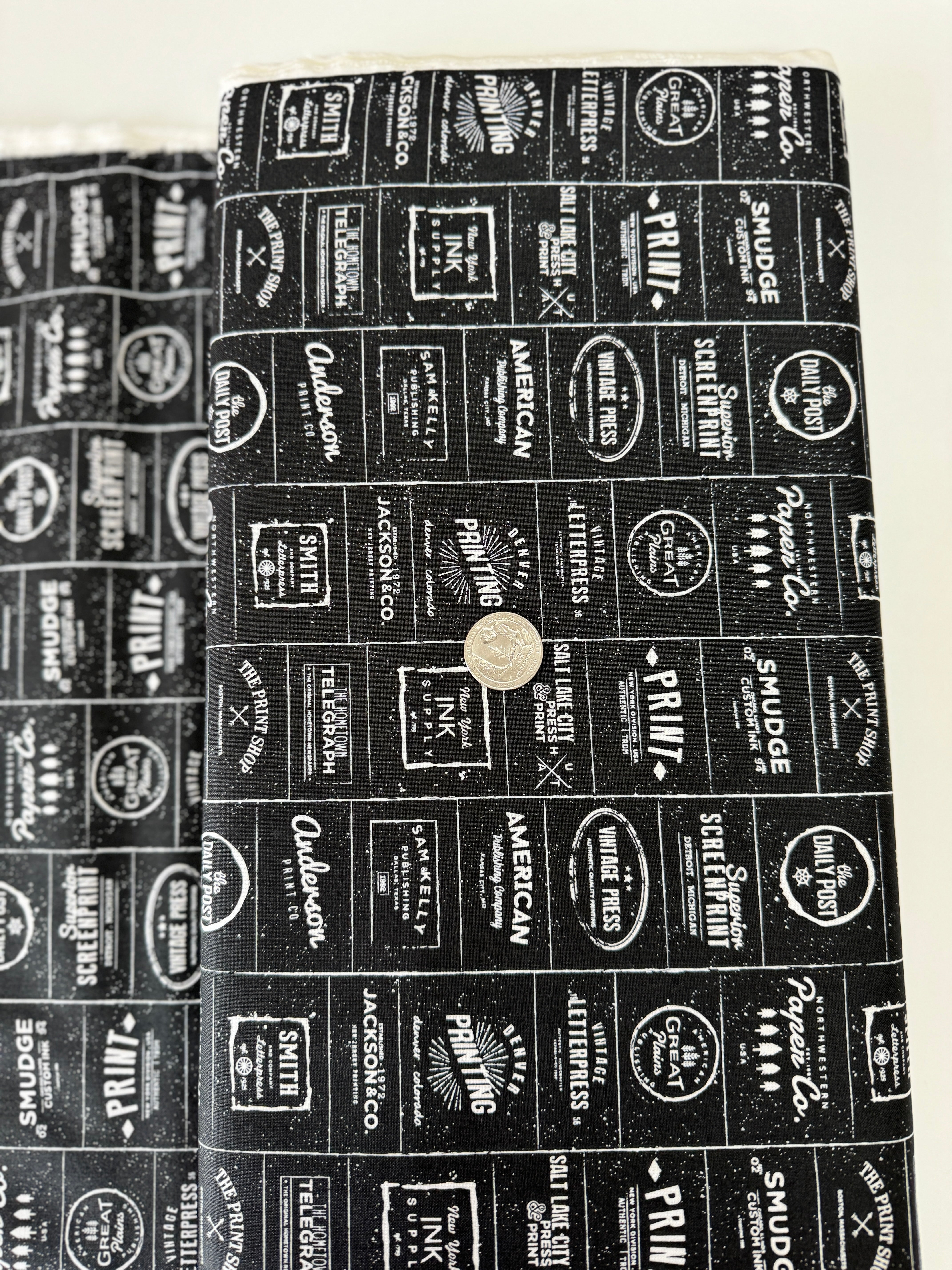 The Print Shop Modern Logos Black fabric by Sweetwater for Moda Fabrics featuring white vintage typography logos on a black background.