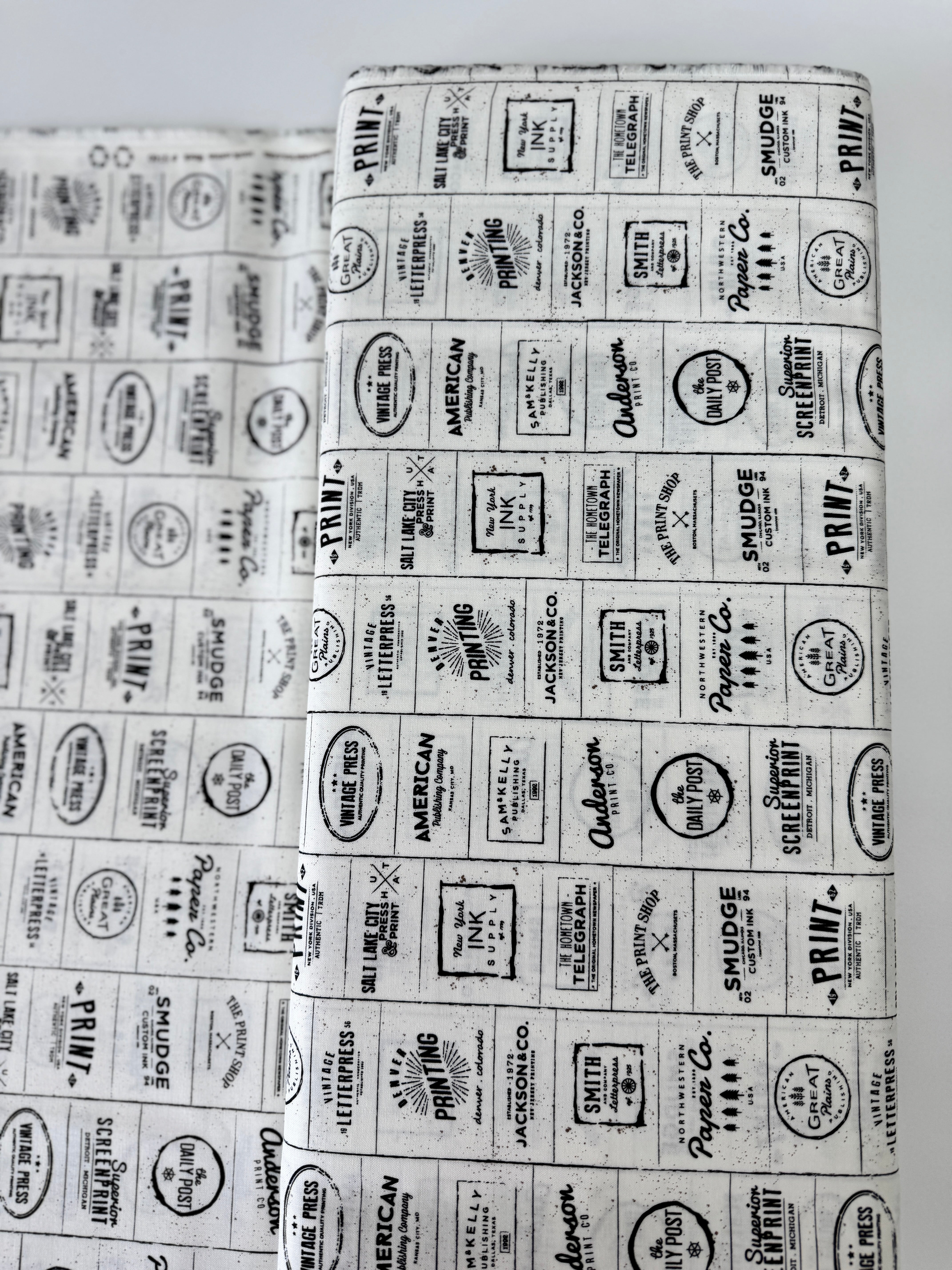 The Print Shop Modern Logos Cream Black fabric by Sweetwater for Moda Fabrics featuring black vintage logo typography on a cream background.