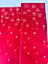 A vibrant red fabric from the Ombre Flurries Metallic collection by V and Co. for Moda Fabrics, featuring shimmering gold metallic snowflakes scattered across the surface.