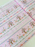 A pastel pink cotton fabric featuring rows of playful deer, white bunnies, trees, and flowers in a stripe pattern - Storybook Forest - Bunnies & Deer Stripe by Timeless Treasures.