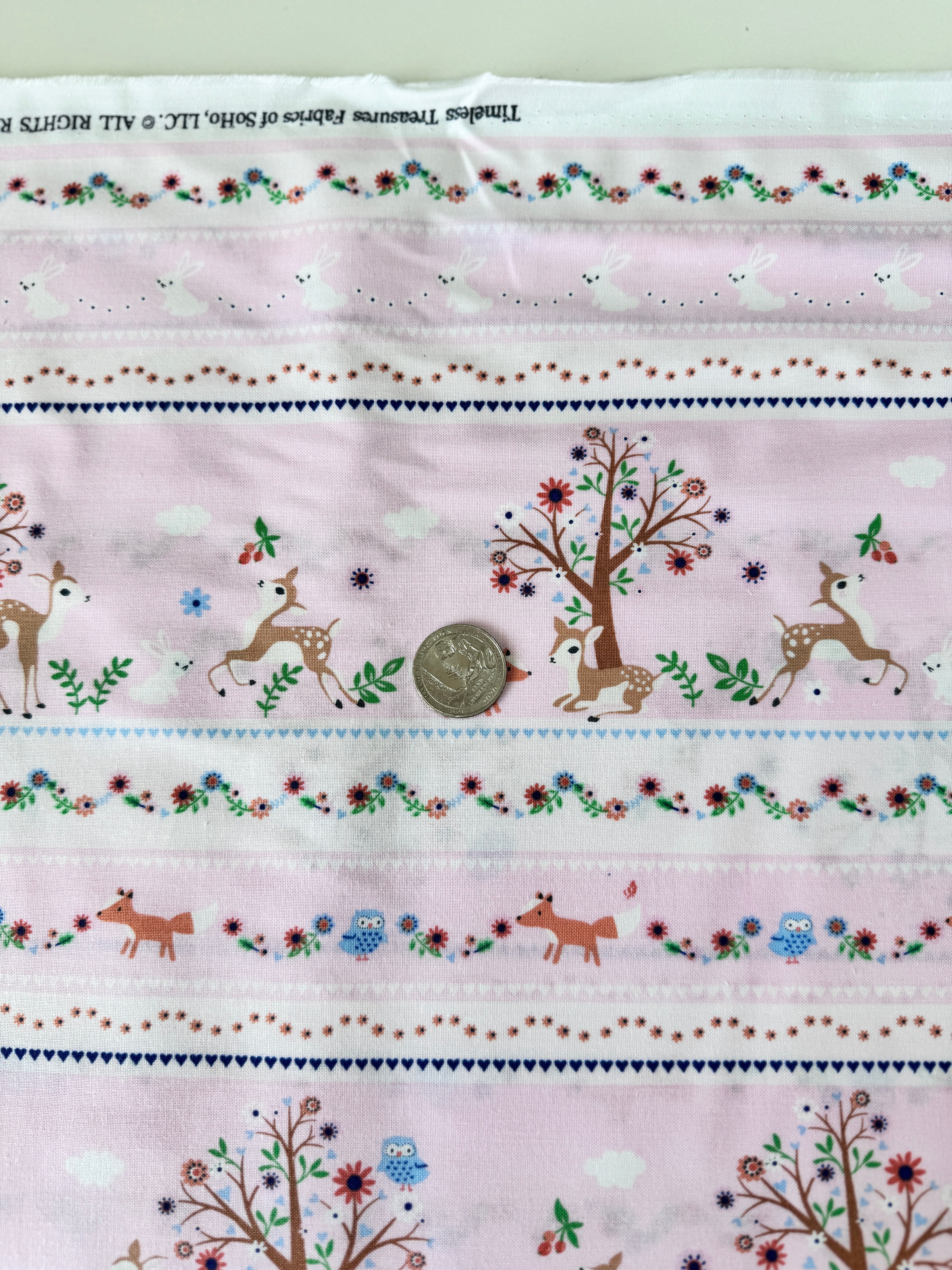 A pastel pink cotton fabric featuring rows of playful deer, white bunnies, trees, and flowers in a stripe pattern - Storybook Forest - Bunnies & Deer Stripe by Timeless Treasures.