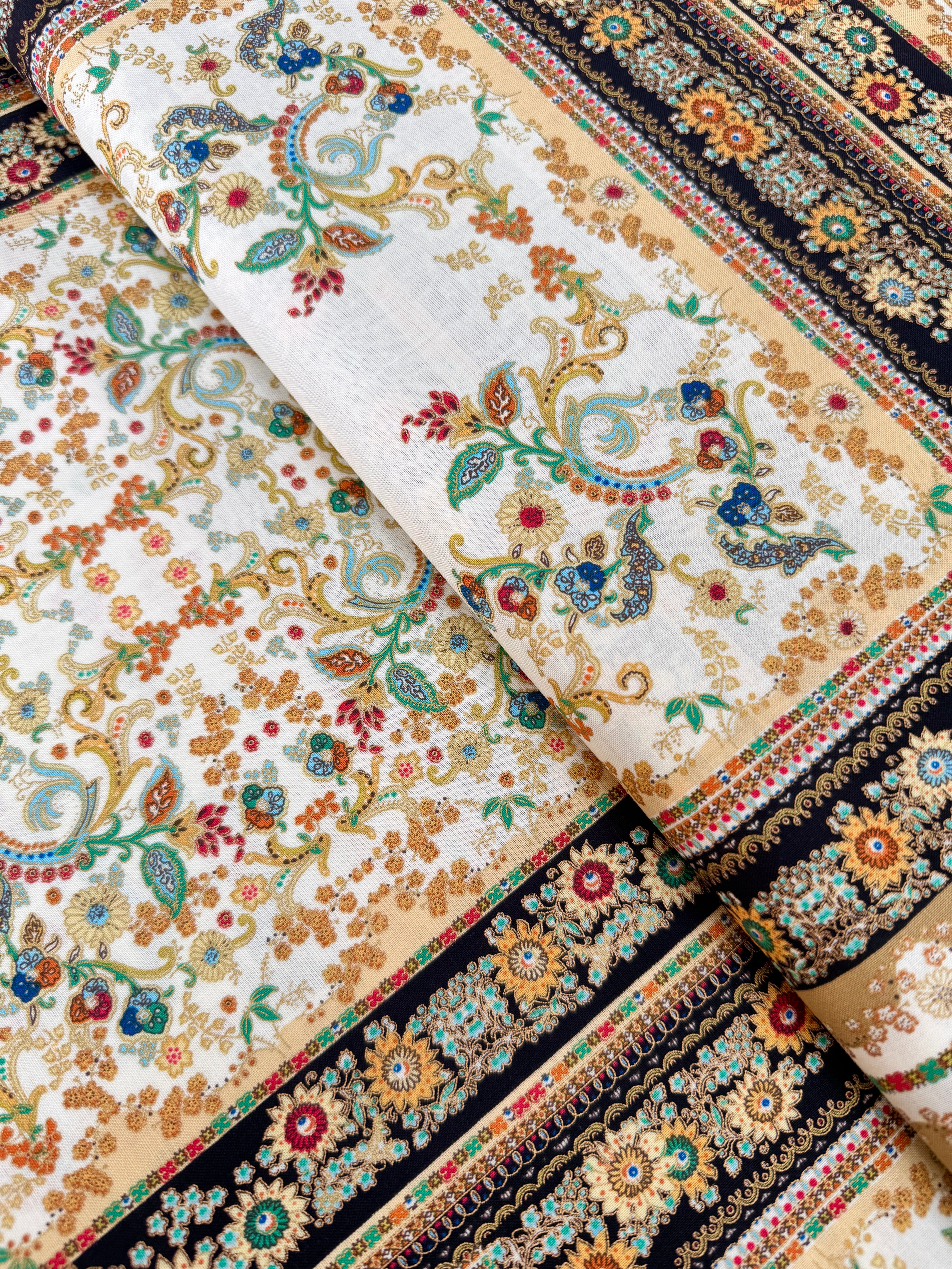 A close-up photo of Hoffman Fabrics’ Antonella Vintage Gold Metallic Fabric showing an ornate floral and scroll tapestry design in gold, cream, and black with shimmering metallic accents.