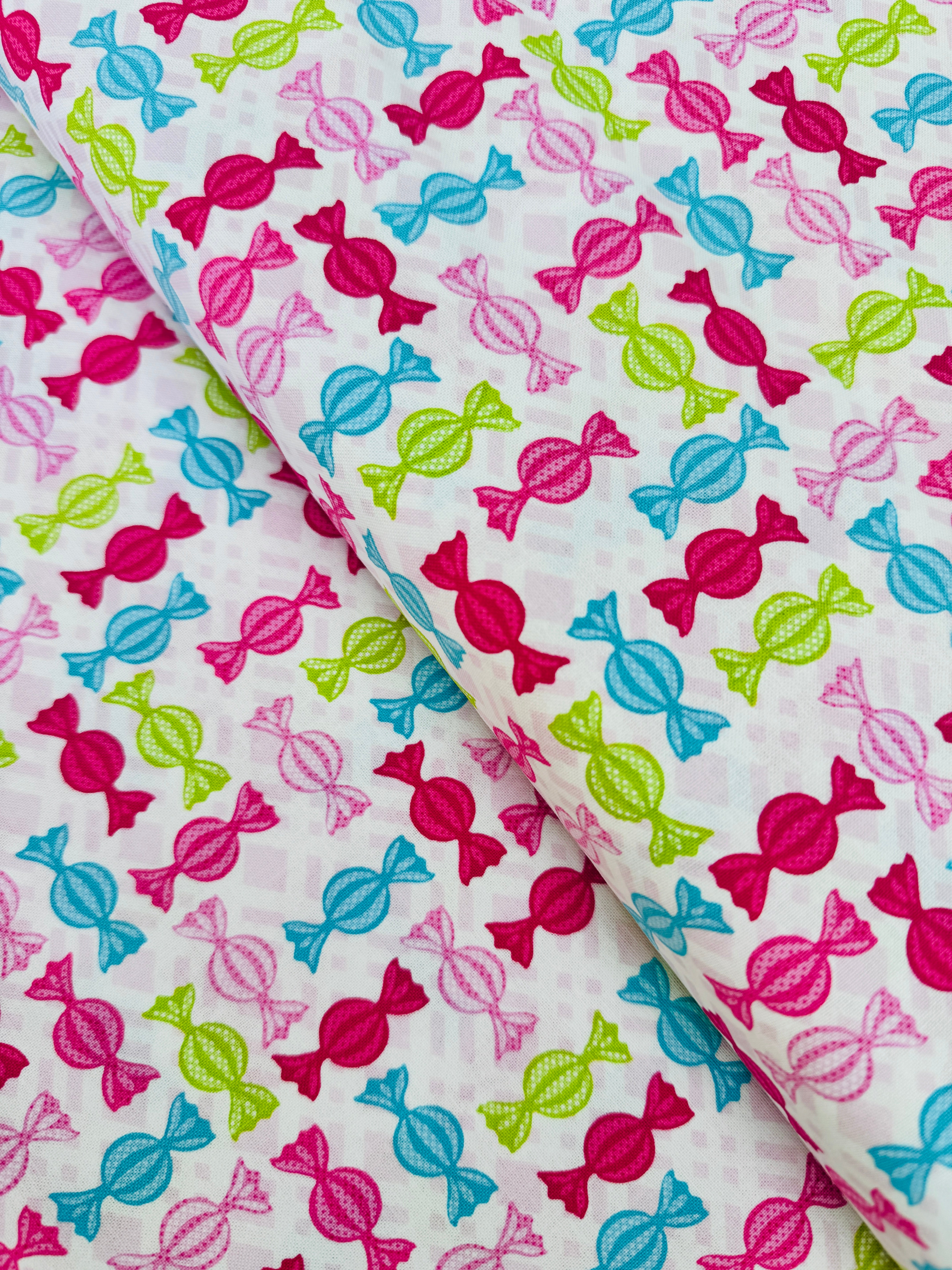 Cupcake Cafe - Wrapped Hard Candies on Pink/White Grid Fabric by Laura Stone for Studio E Fabrics featuring colorful candy motifs on a pink and white lattice background.