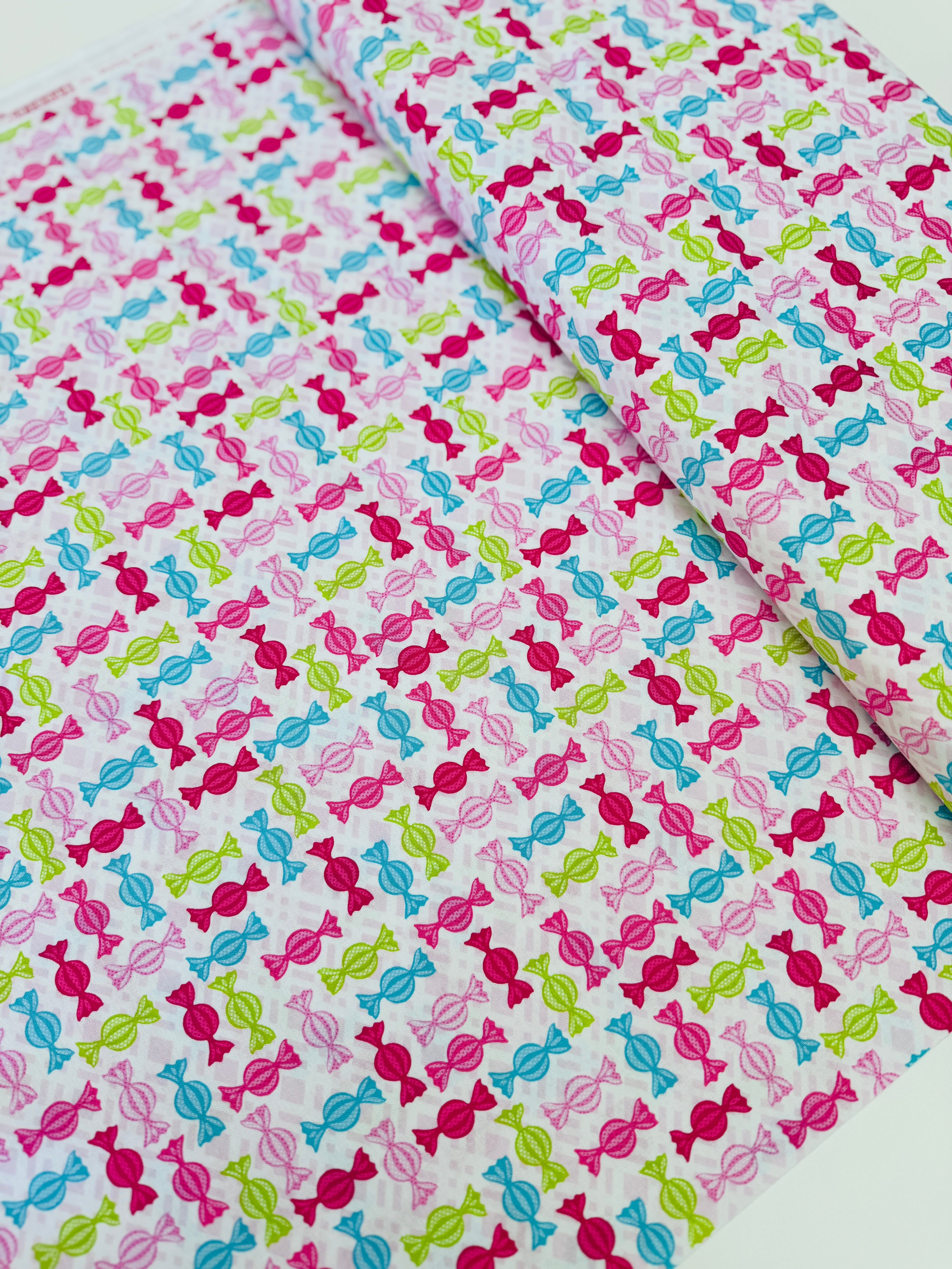 Cupcake Cafe - Wrapped Hard Candies on Pink/White Grid Fabric by Laura Stone for Studio E Fabrics featuring colorful candy motifs on a pink and white lattice background.
