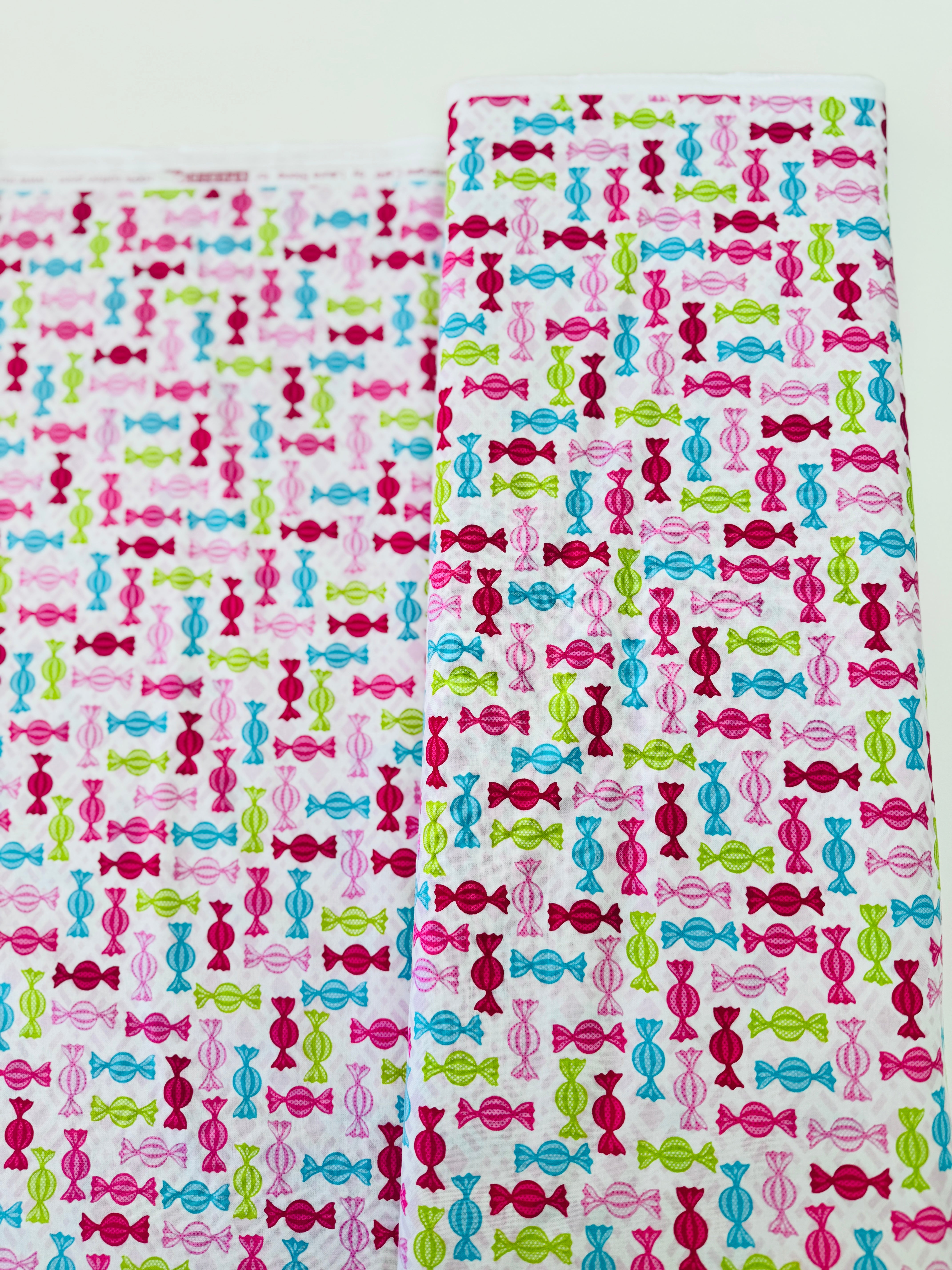 Cupcake Cafe - Wrapped Hard Candies on Pink/White Grid Fabric by Laura Stone for Studio E Fabrics featuring colorful candy motifs on a pink and white lattice background.