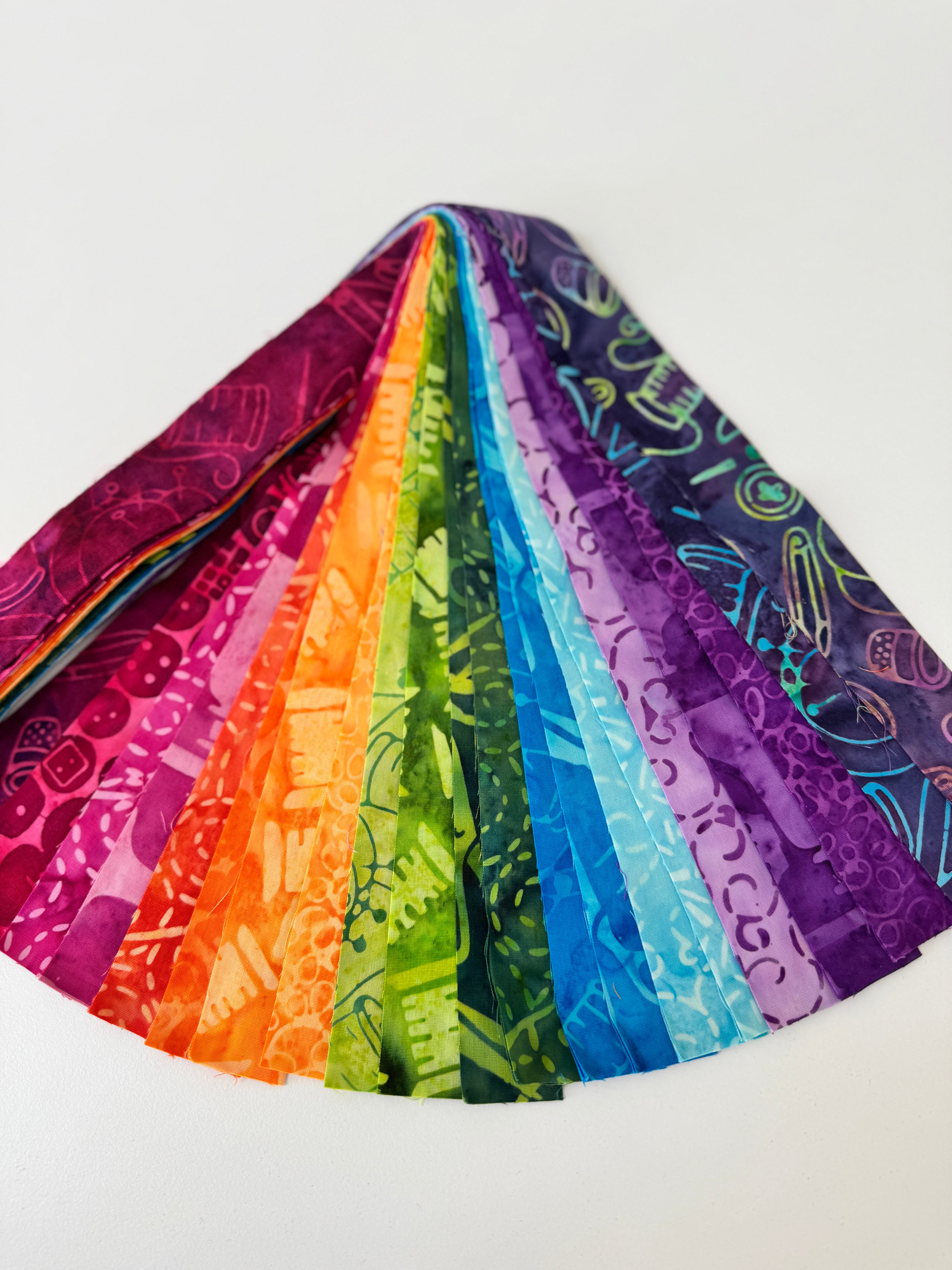 Assorted rainbow batik fabric strips fanned out, featuring 21 colorful 2-inch strips by Kathy Engle for Island Batik.