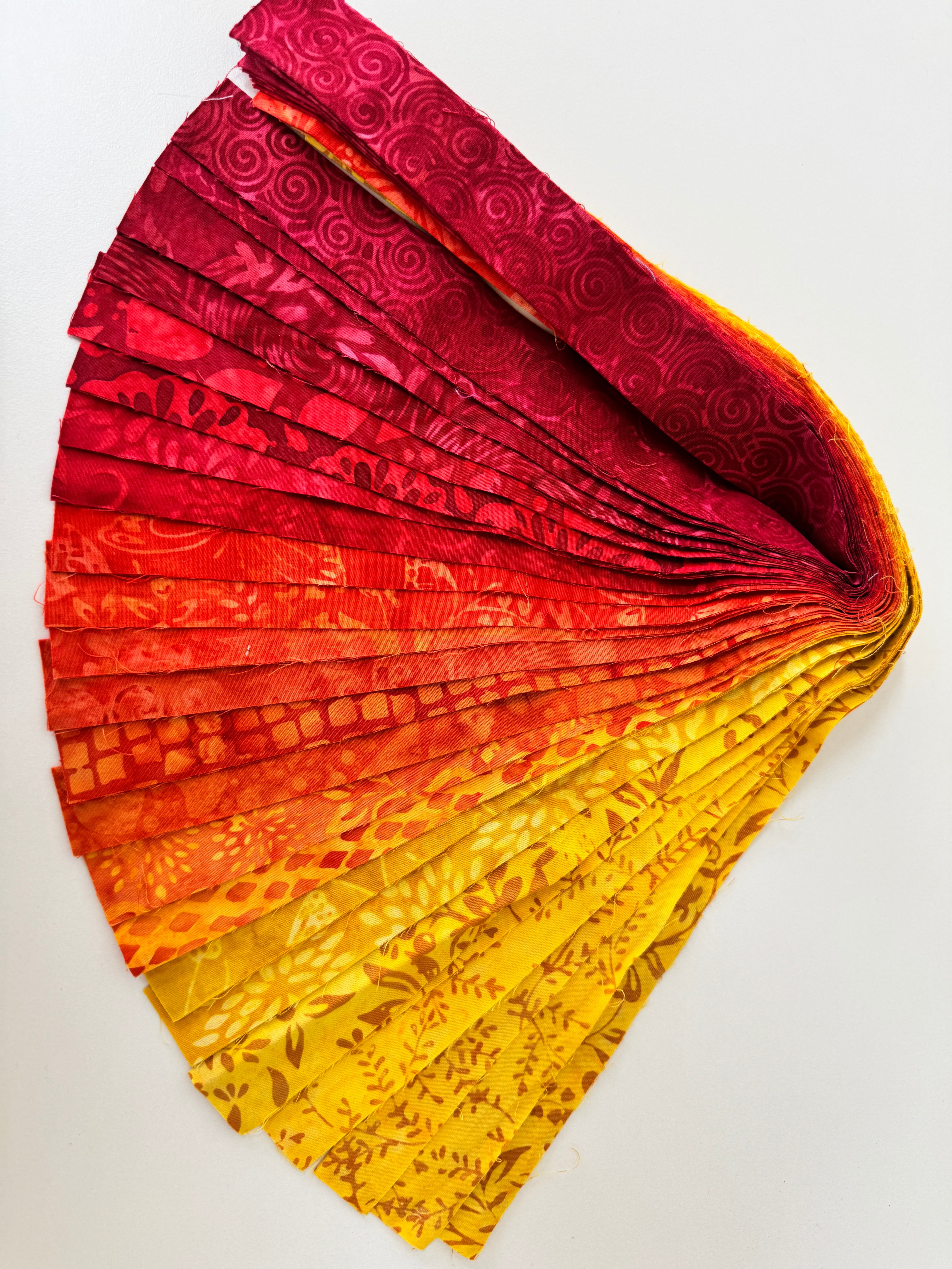 Bundle of assorted flame-colored batik fabric strips in red, orange, and yellow shades arranged in a fan layout.
