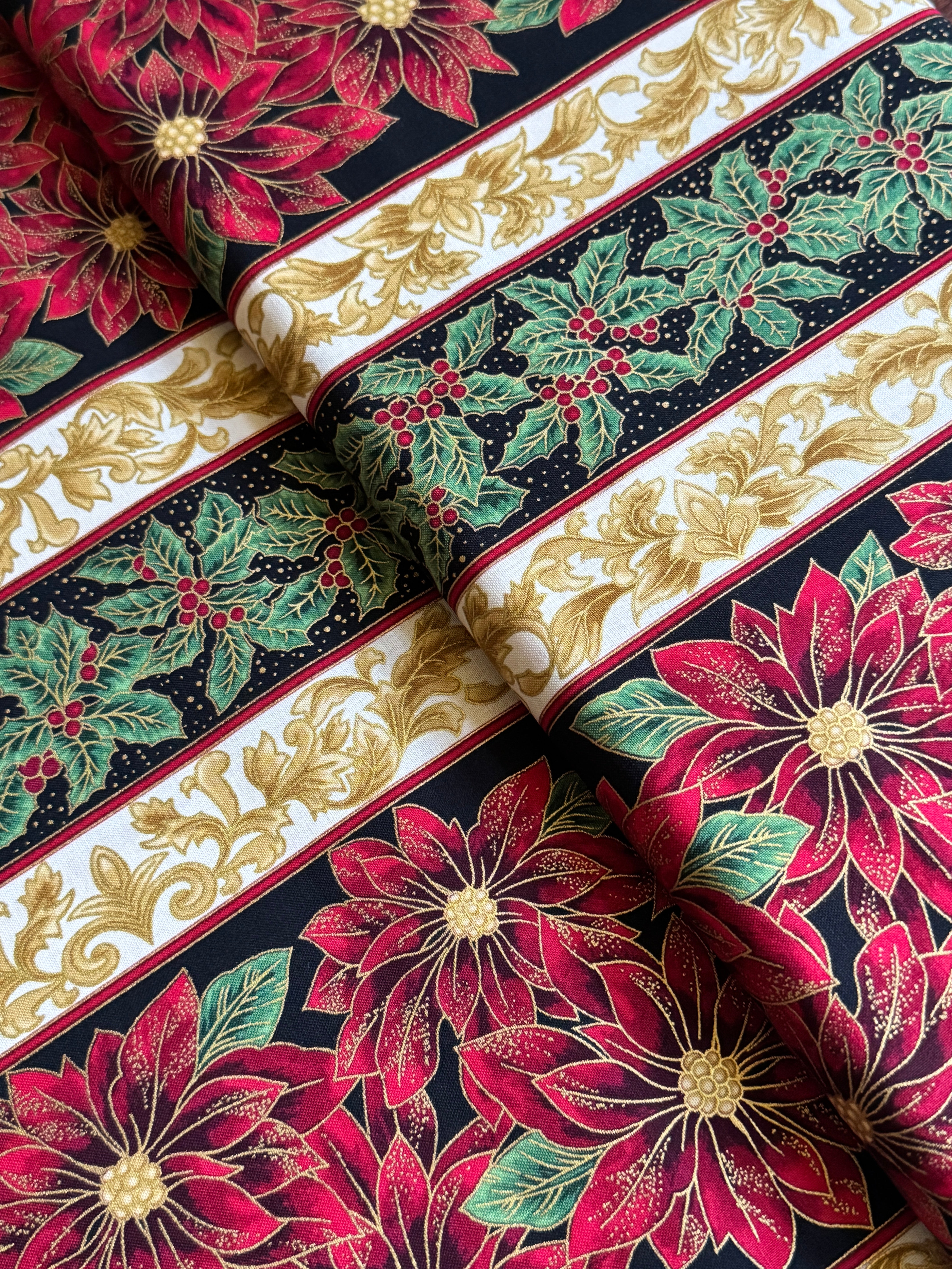 Holiday Flourish 12 poinsettia stripe black metallic fabric featuring red poinsettias, holly leaves, and gold scrollwork by Peggy Toole for Robert Kaufman.