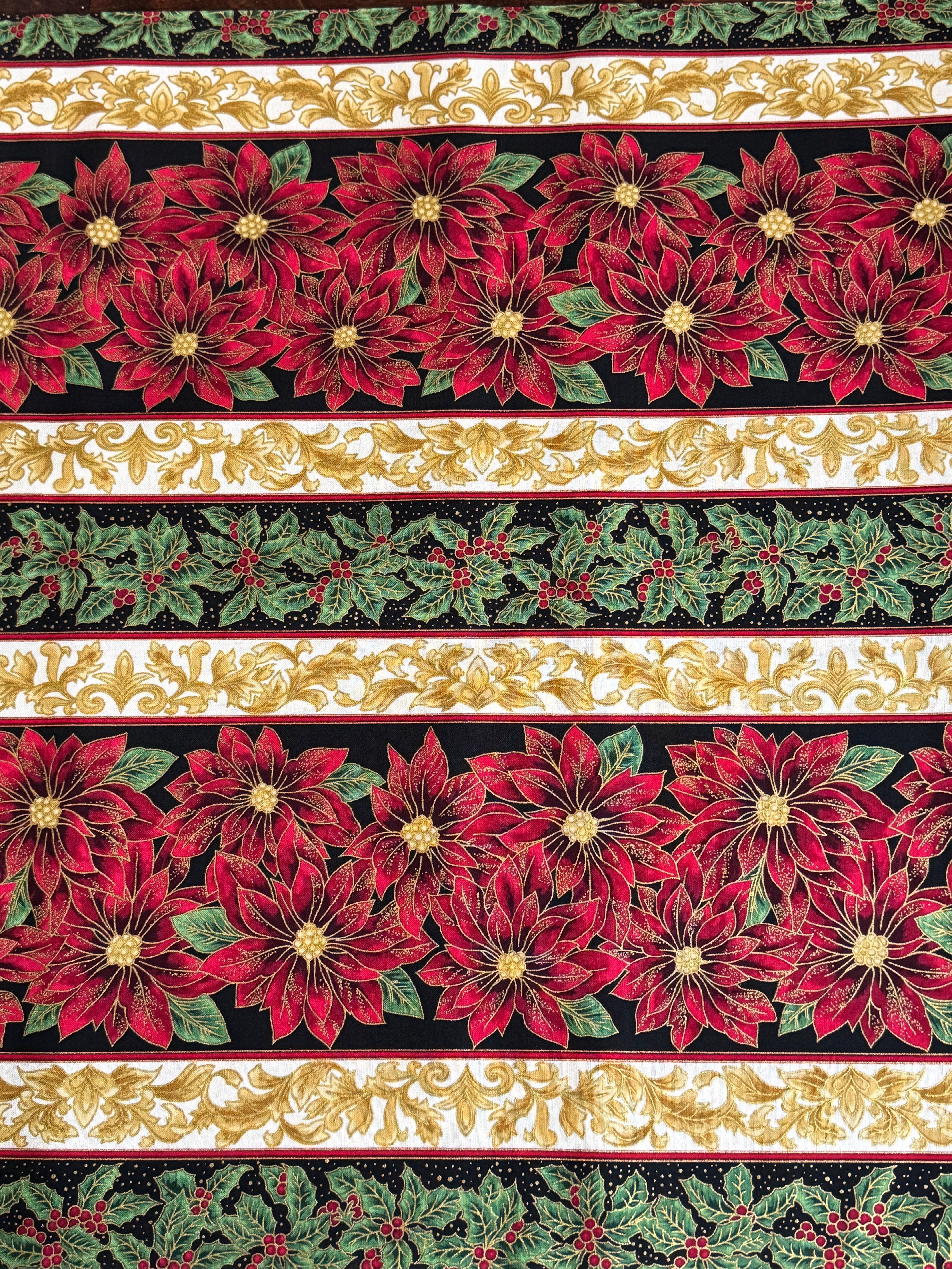 Holiday Flourish 12 poinsettia stripe black metallic fabric featuring red poinsettias, holly leaves, and gold scrollwork by Peggy Toole for Robert Kaufman.