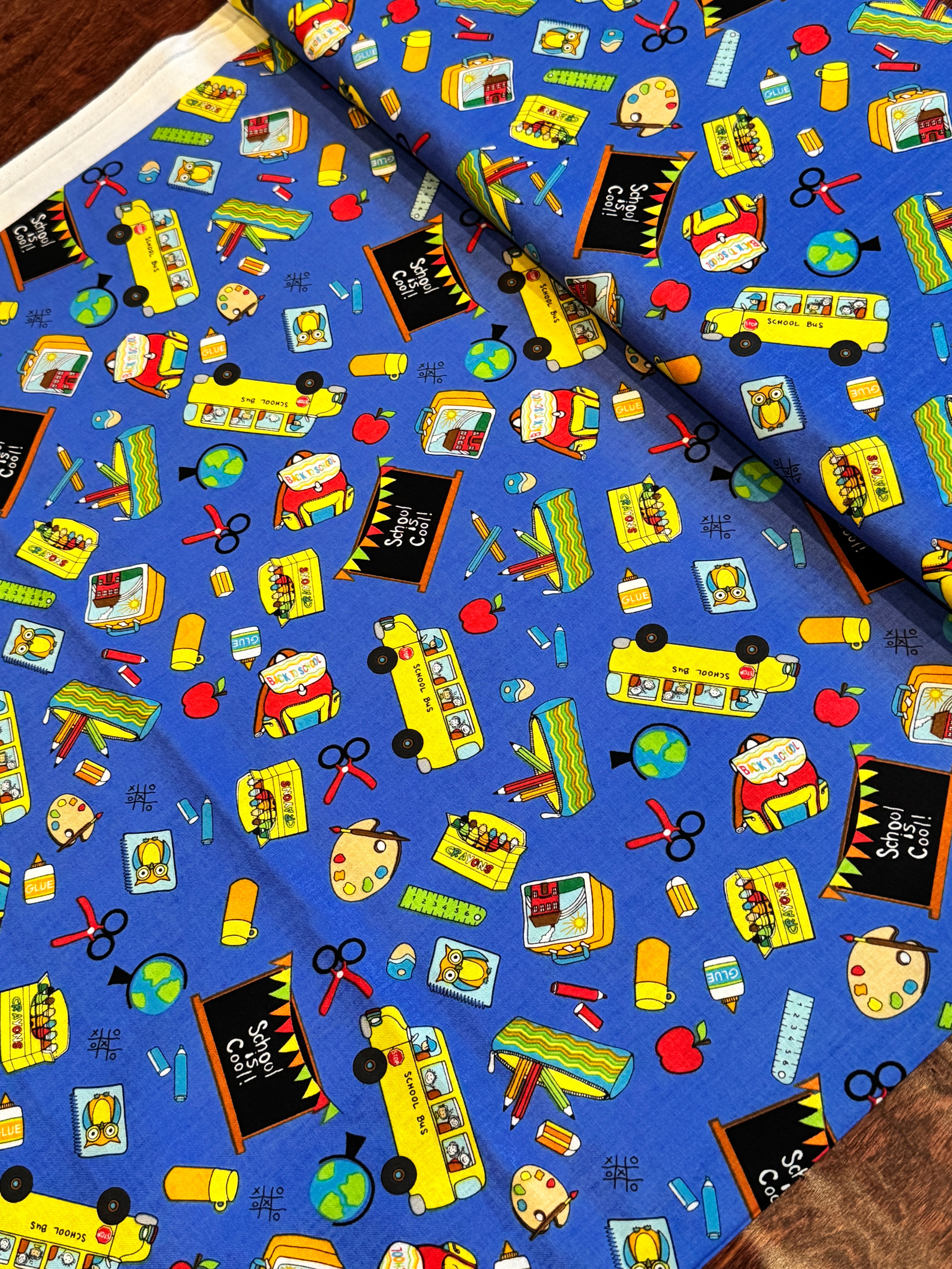Blue School Rules cotton fabric featuring school buses, crayons, apples, chalkboards and classroom supplies by Blank Quilting.
