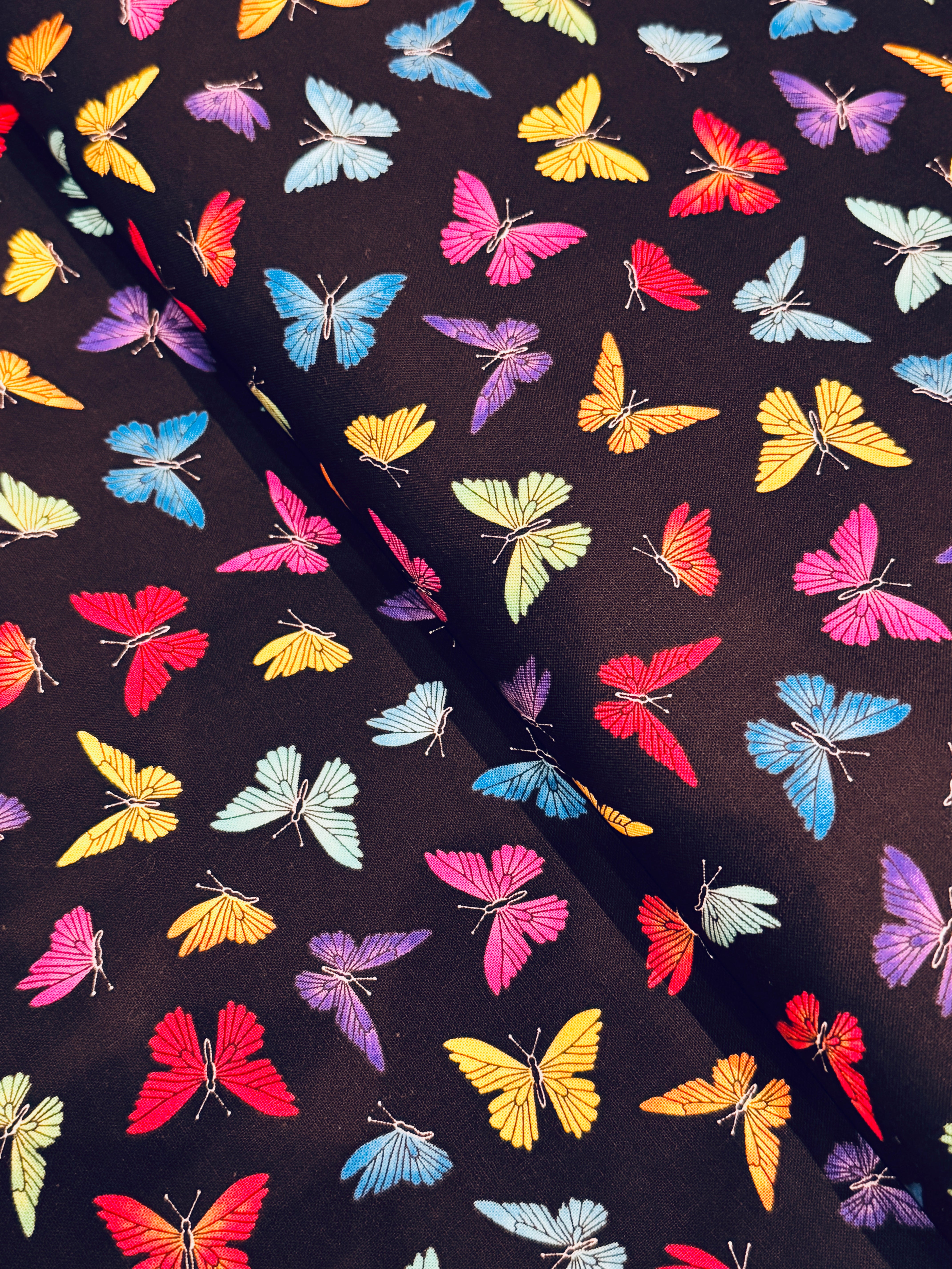 Colorful rainbow butterflies scattered on a black background fabric by Chong-A Hwang for Timeless Treasures.
