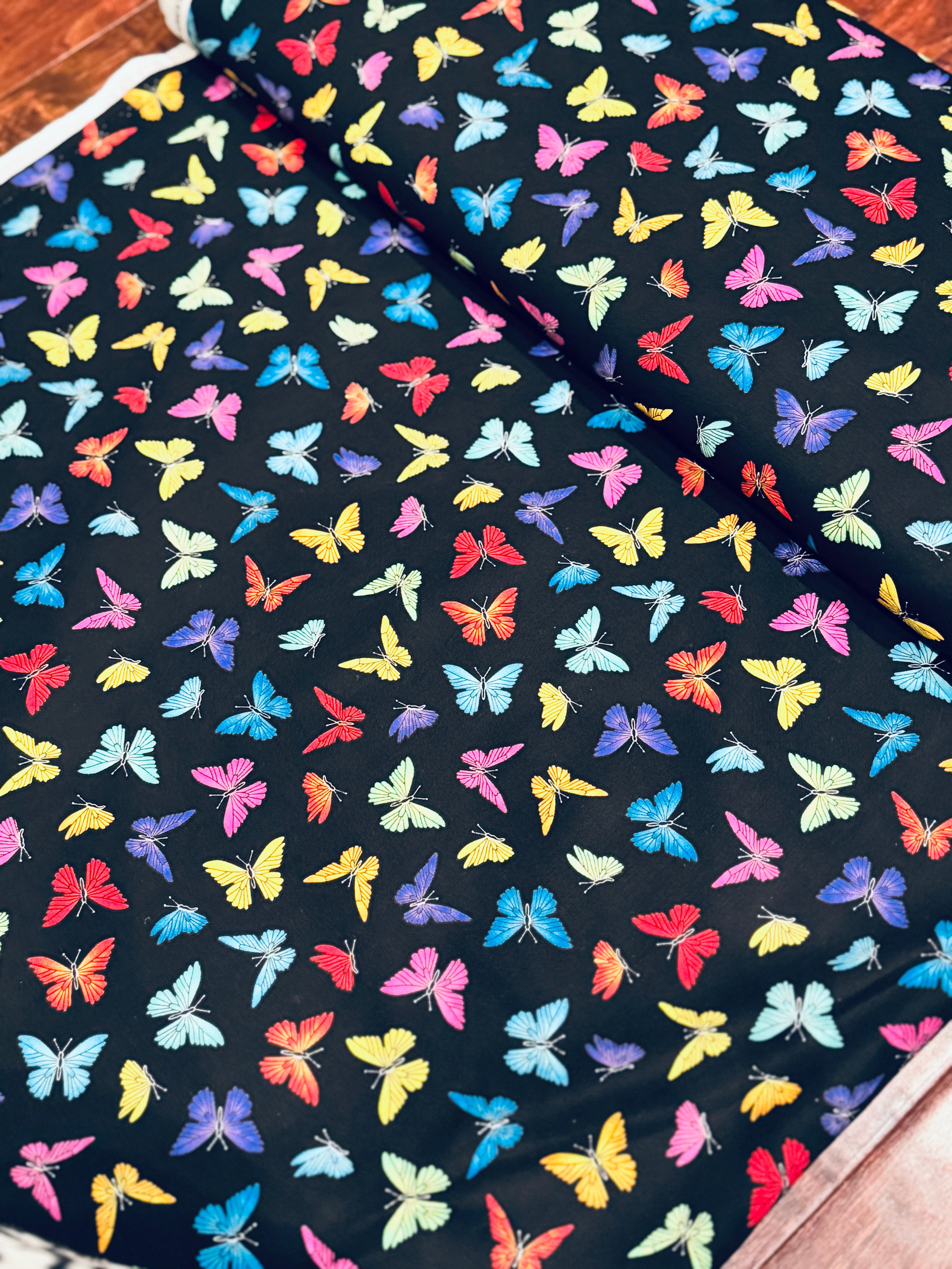 Colorful rainbow butterflies scattered on a black background fabric by Chong-A Hwang for Timeless Treasures.