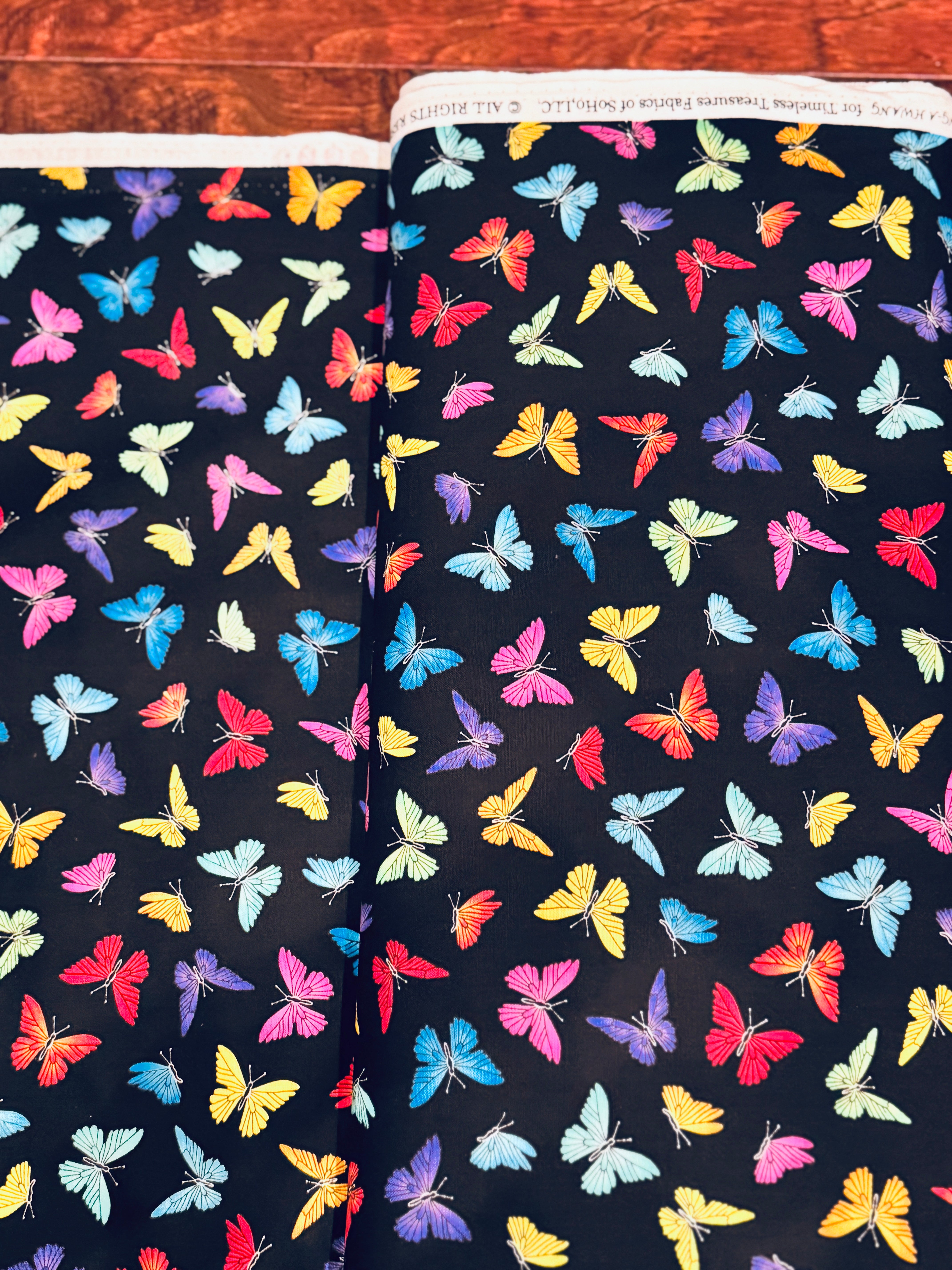 Colorful rainbow butterflies scattered on a black background fabric by Chong-A Hwang for Timeless Treasures.