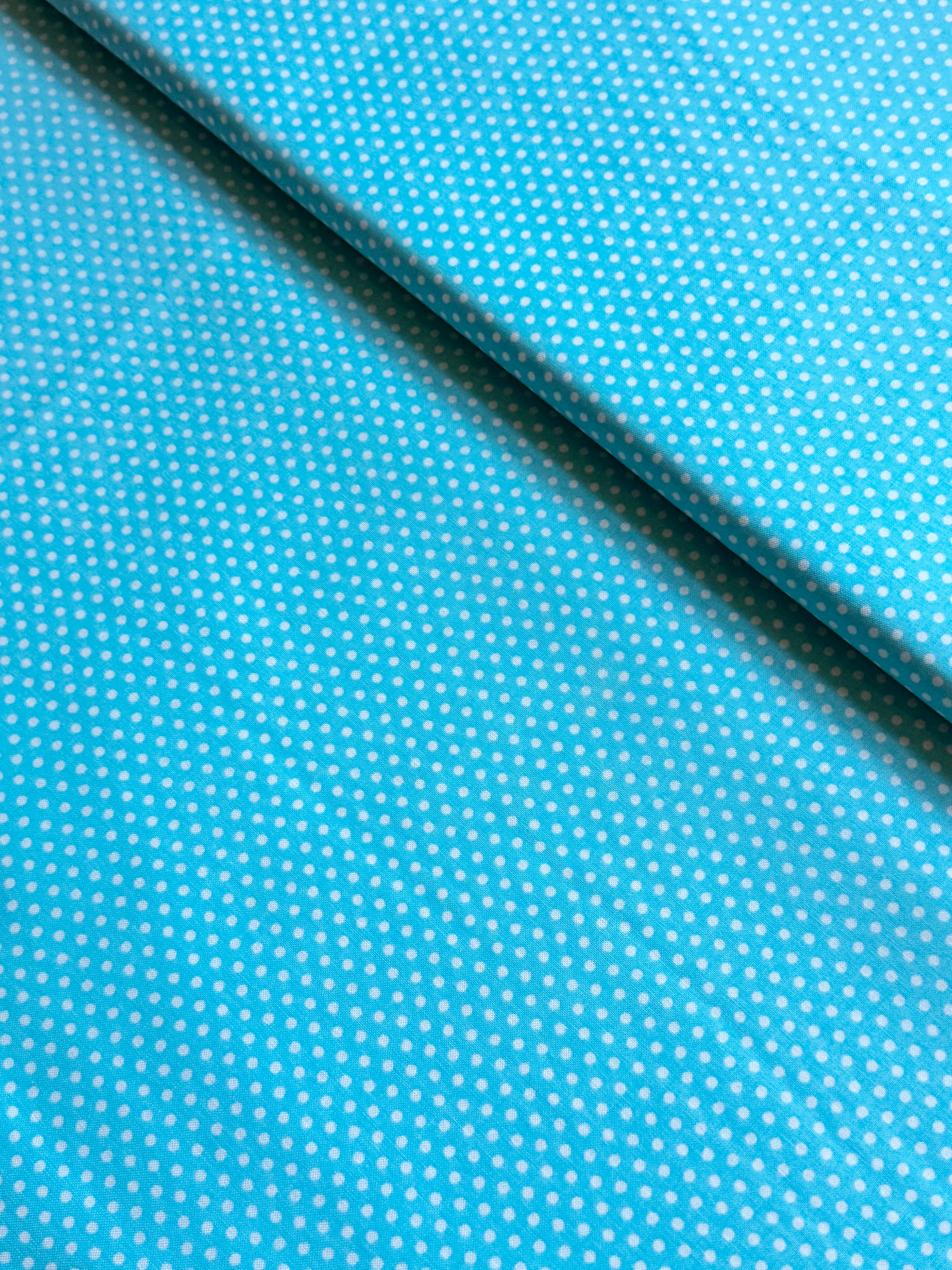 Aqua blue cotton fabric featuring small white polka dots in an all-over pattern by Robert Kaufman Fabrics, ideal for quilting, sewing, nursery décor, and craft projects.