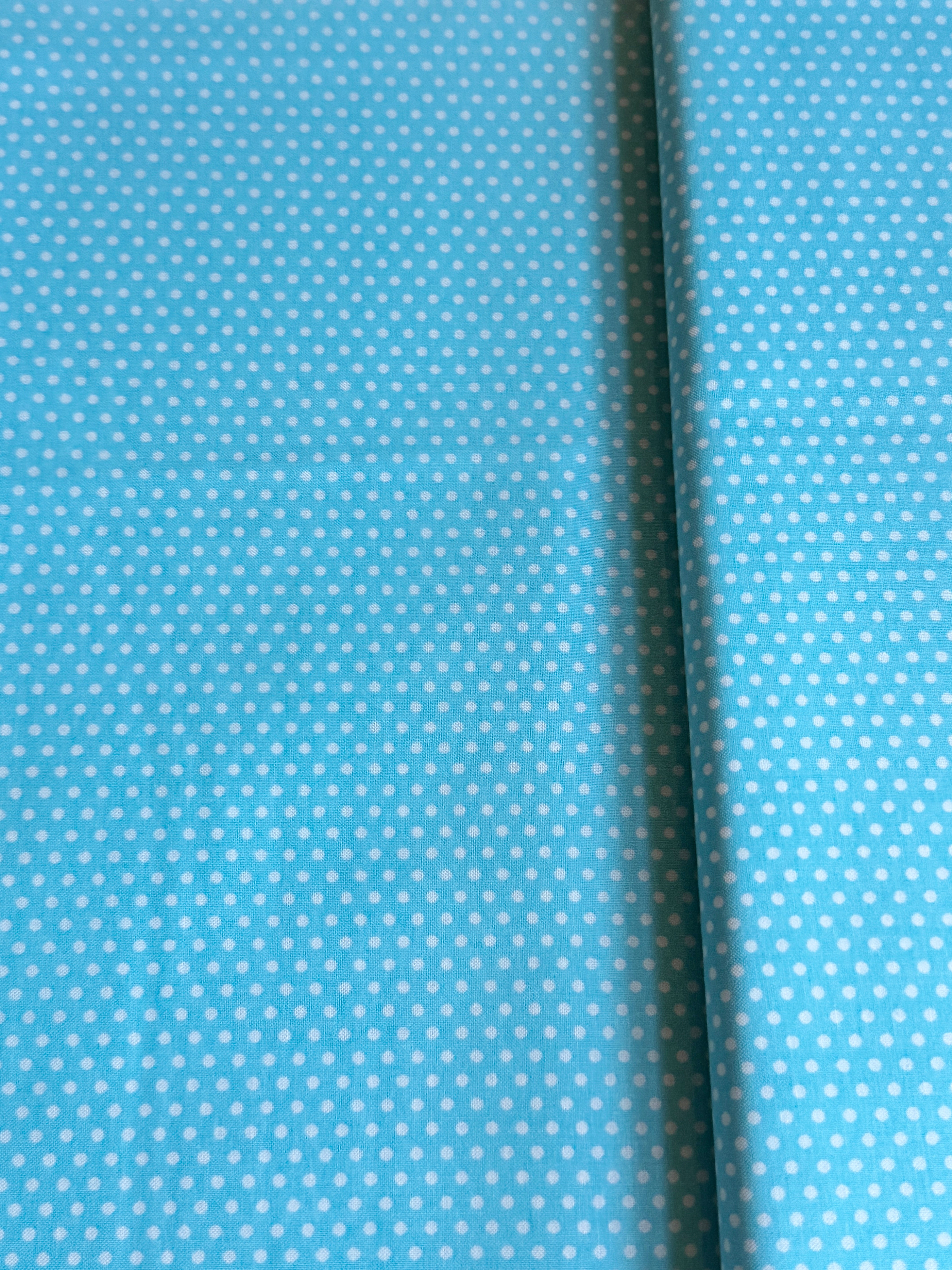 Aqua blue cotton fabric featuring small white polka dots in an all-over pattern by Robert Kaufman Fabrics, ideal for quilting, sewing, nursery décor, and craft projects.