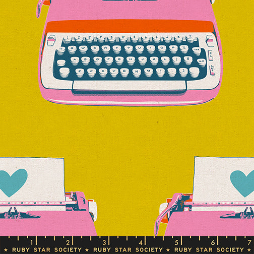 Close-up of Ruby Star Society’s Best Day Ever Typewriters Golden Canvas fabric by Melody Miller for Moda Fabrics, featuring colorful retro typewriters in pink, teal, and orange with heart-shaped papers on a mustard yellow background.