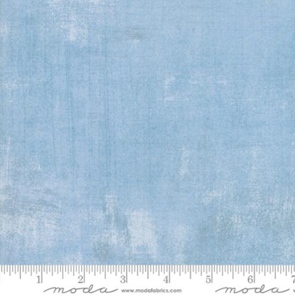 A close-up image of Grunge Cosmic Quilt Back fabric by BasicGrey for Moda Fabrics, featuring a soft light blue color with a subtle textured grunge pattern.