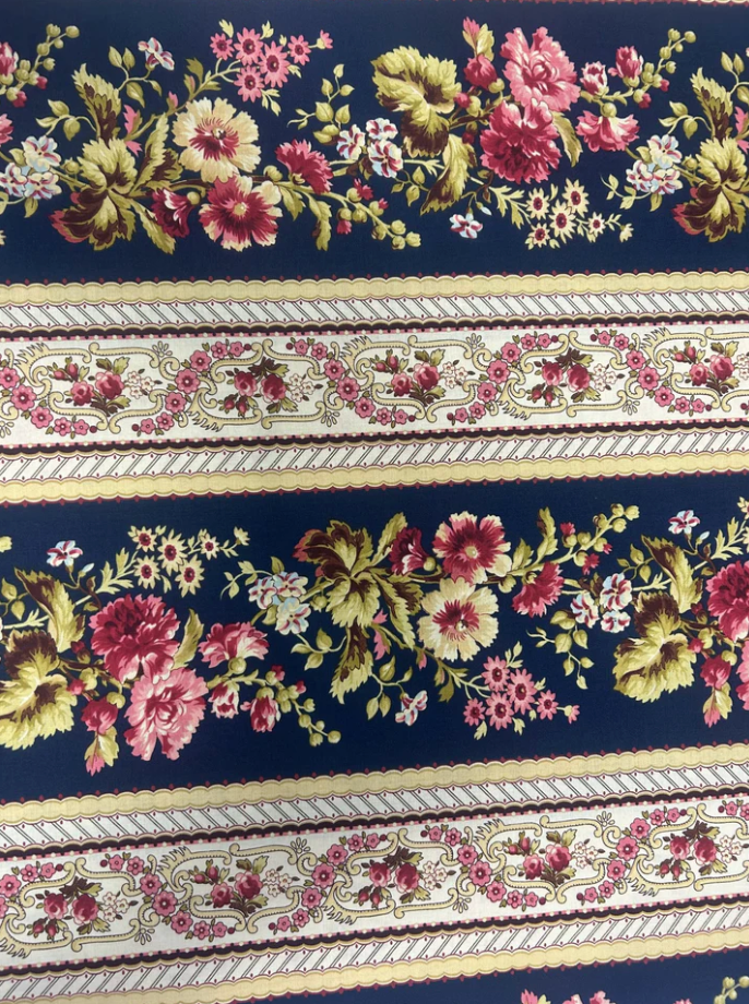 Bricolage Navy Border Stripe fabric by Kaye England for Wilmington Prints featuring elegant floral garlands and decorative border stripes in pink, burgundy, cream, and green on a rich navy background.