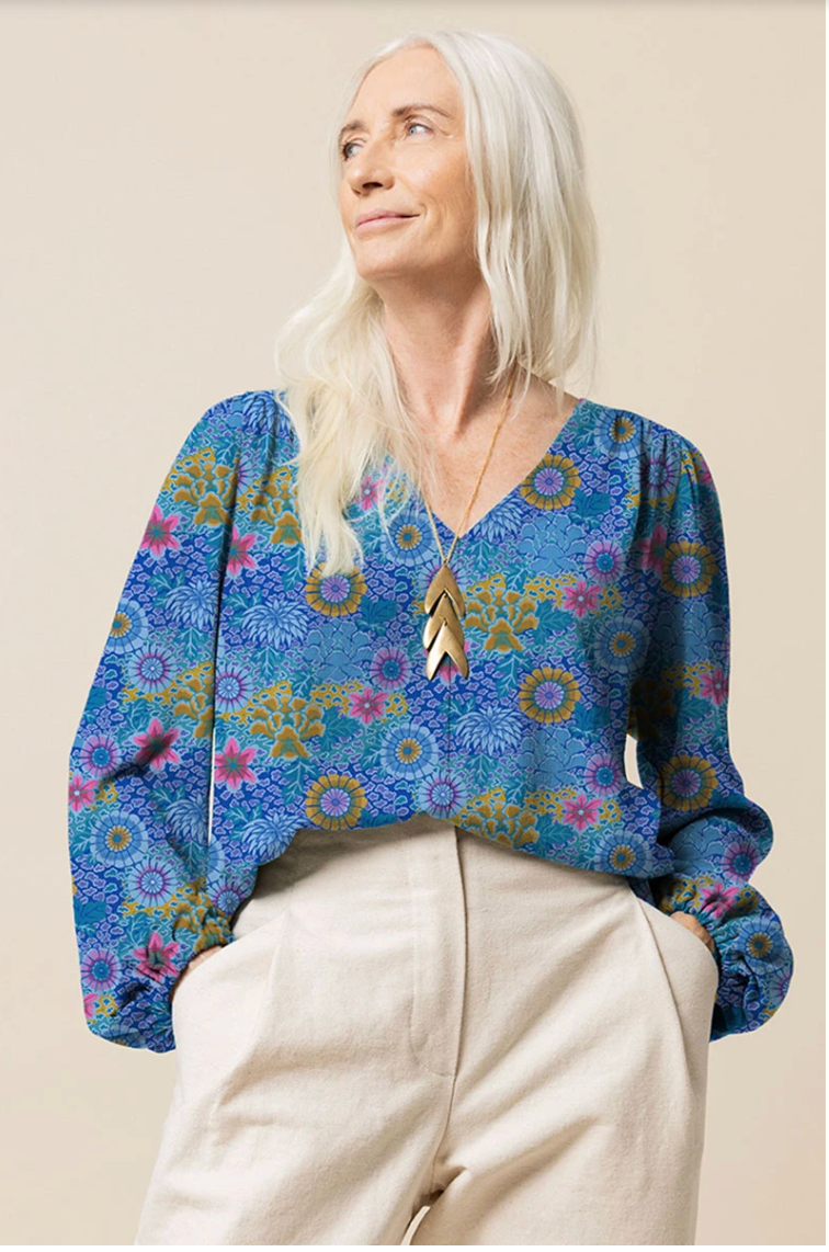 Woman wearing a blouse made with Kaffe Fassett Dream Blue cotton lawn fabric, featuring colorful blue, aqua, pink, and gold floral motifs.