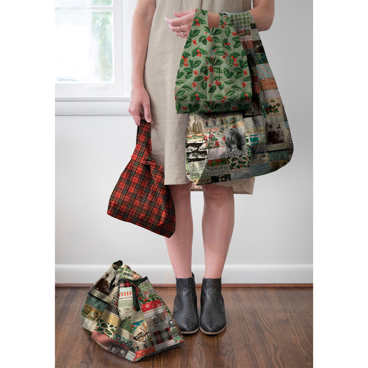 Handmade reusable shopping bags and decorative throw pillows sewn from Tim Holtz Christmas Holly canvas fabric displayed in a cozy vintage-inspired holiday setting.